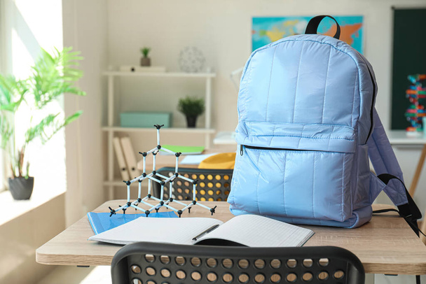 Backpack with notebooks and molecular model on desk in classroom - Photo, Image