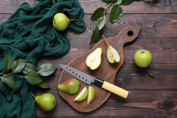 Tablero con peras en rodajas y cuchillo sobre mesa de madera oscura - Foto, imagen