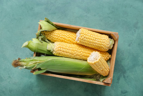 Wooden box with fresh corn cobs on green table - Photo, Image