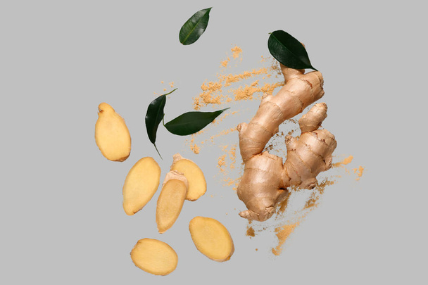 Flying slices of fresh ginger root with dried powder and leaves on grey background - Photo, image