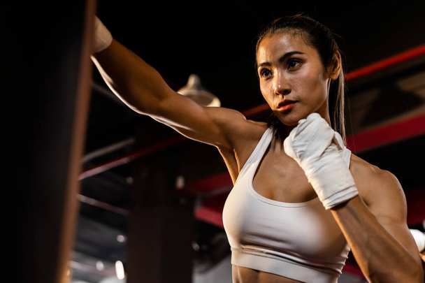 Aziatische vrouwelijke Muya Thai bokser training, gewikkelde hand ponsen op schoppen tas in de sportschool. Gezonde sport- en fitnesslevensstijl, kracht- en conditietraining voor bokswedstrijden. Impetus - Foto, afbeelding