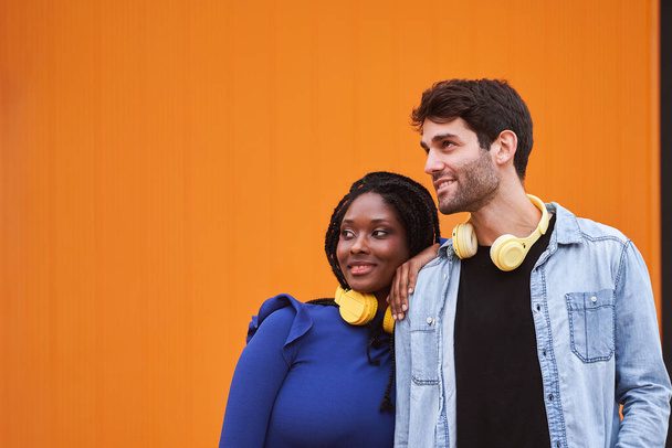 Couple multi-ethnique avec écouteurs regardant l'infini debout sur fond coloré. Concept de relation. - Photo, image