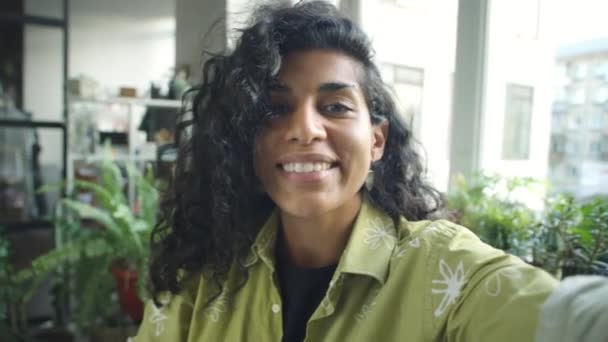 POV mladé hispánské ženy mávající a chatování na kameru při práci v kanceláři zdobené rostlinami - Záběry, video