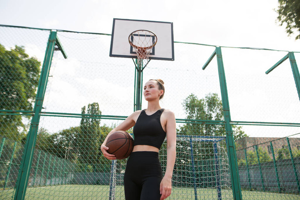 Jong sportmeisje met een basketbal op het basketbalveld buiten, actief weekend. - Foto, afbeelding