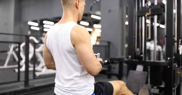 El culturista masculino entrena levantando pesas en el simulador en el gimnasio. Atleta haciendo ejercicio en el gimnasio - Metraje, vídeo