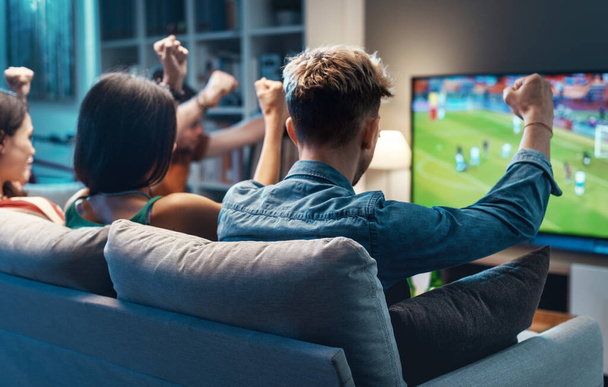 Group of young friends watching a football match on TV together and cheering for their team - Фото, изображение