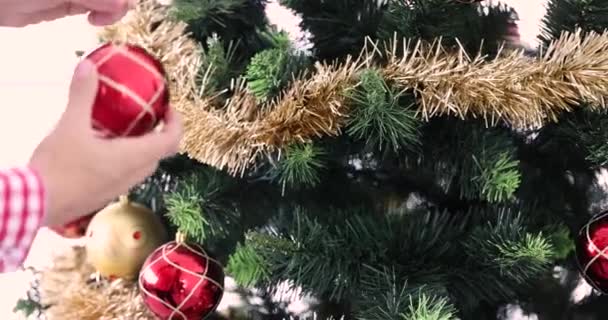 女性の手はクリスマスツリーのクローズアップに赤いクリスマスのおもちゃを掛けます. 新しい年のコンセプトの準備 - 映像、動画