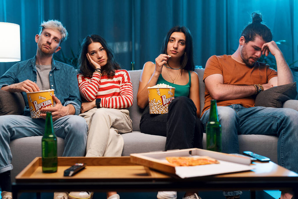 Vrienden zitten op de bank en kijken samen naar een saaie film op tv - Foto, afbeelding