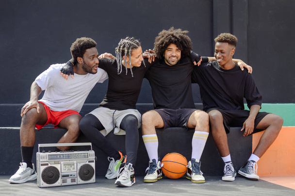 Skupina multietnických mužů a žen ve sportovním oblečení sedí na basketbalovém hřišti a dívají se na sebe - Fotografie, Obrázek
