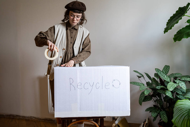 Öko-aktivista otthon áll, whiskyt tart, régi ruhákat pakol, cipőt kartondobozban újrahasznosít, ruhatárat takarít, ruhákat küld az újrahasznosító központba. Környezetbarát otthon. Bolygó megmentése - Fotó, kép