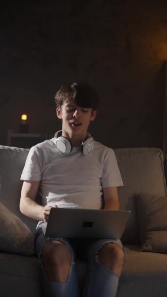 Leuke tienerjongen die 's nachts op de laptop praat terwijl hij op de bank zit. Jongeren met videogesprekken thuis. - Video