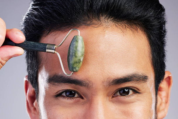 Man, portrait or face massage with roller or quartz product for healthy skincare on studio background. Forehead, crystal stone treatment or male model with facial dermatology cosmetic for beauty glow. - Foto, Imagen