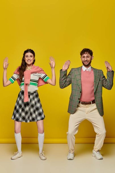 funny couple, happy young man and woman gesturing, standing on yellow backdrop, looking at camera - Foto, immagini