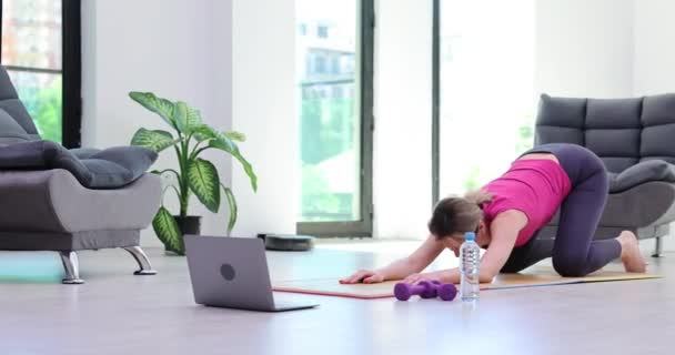 Gericht gemotiveerd meisje zit op de vloer met laptop uit te rekken hand en leunen. Sterke fysiek gezonde vrouw en online fitness en stretching flexibiliteit yoga - Video