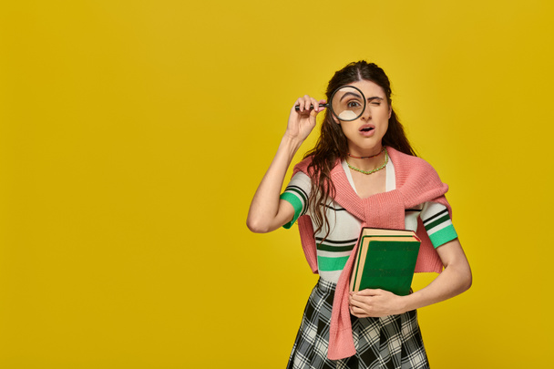 estudiante curioso sosteniendo libros y lupa, zoom, descubrimiento, mujer joven en traje de la universidad, amarillo - Foto, Imagen