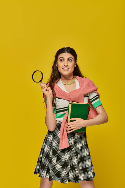 Любопытная молодая женщина с книгами и увеличителем, зум, открытие, студентка в униформе колледжа, улыбка - Фото, изображение
