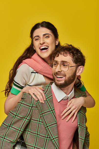 funny students, cheerful man piggybacking young woman on yellow backdrop, college outfits, couple - Fotografie, Obrázek