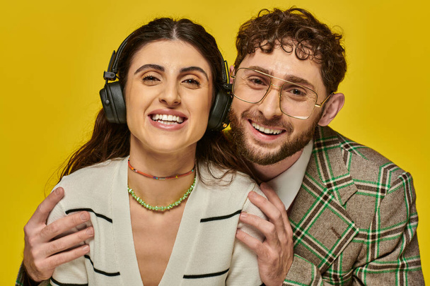 estudiantes universitarios, mujer feliz en auriculares escuchando música cerca de hombre barbudo, divertido y alegre - Foto, Imagen
