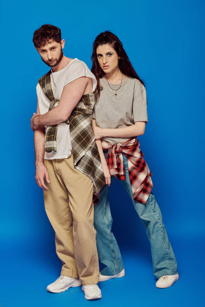 couple posing in street wear, blue backdrop, woman with bold makeup standing with bearded man, style - Photo, Image
