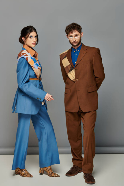 trendy couple, fashion shoot, man and woman in suits posing on grey backdrop, brown, blue, style - Photo, Image