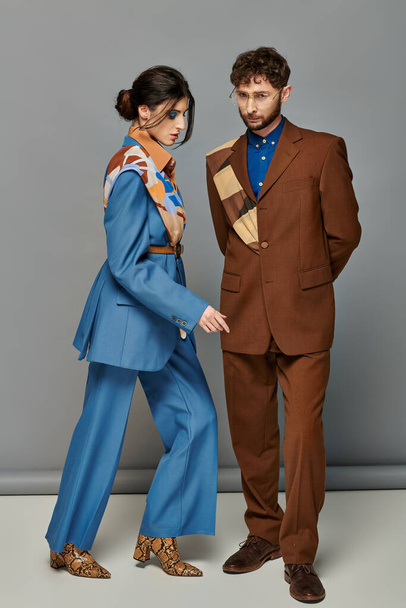 couple à la mode, homme et femme en costumes posant sur fond gris, brun, bleu, tournage de mode - Photo, image
