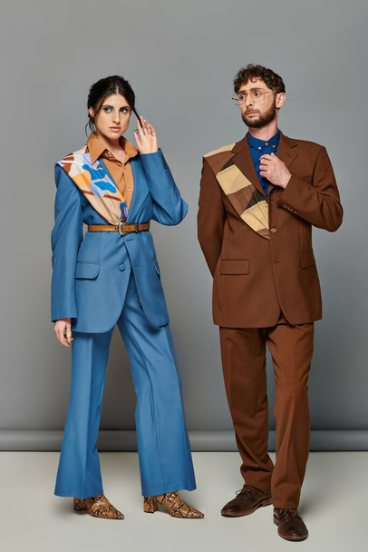 man en vrouw met baard in pakken op maat poseren op grijze achtergrond, bruin, blauw, fashion shoot, koppel - Foto, afbeelding