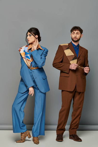 man en vrouw in maatpakken, staande op grijze achtergrond, fashion shoot, huisstijl, koppel - Foto, afbeelding