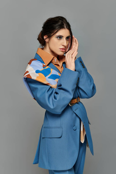 Porträt, brünette Frau mit kühnem Make-up, verträumt, Modell im blauen Anzug, formelle Kleidung, grauer Hintergrund - Foto, Bild