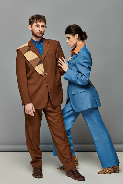 trendy pose, models in formal attire on grey background, man and woman in suits, fashion shoot - Foto, Imagen