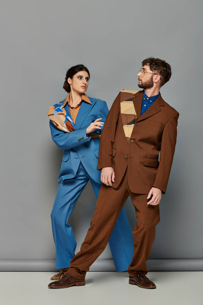 μοντέλα μόδας με κοστούμια που ποζάρουν σε γκρι φόντο, chic άντρας και γυναίκα κοιτάζονται μεταξύ τους - Φωτογραφία, εικόνα
