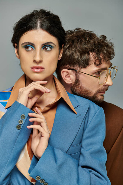 Trendpaar posiert auf grauem Hintergrund, Anzüge, eleganter Stil, Frau mit kühnem Make-up, bärtiger Mann - Foto, Bild
