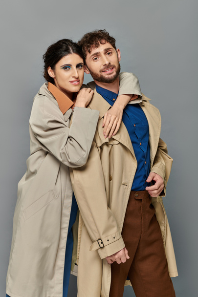 herfst seizoen, glimlach, man en vrouw knuffelen op grijze achtergrond, koppel in trench jassen, stijl, romantiek - Foto, afbeelding