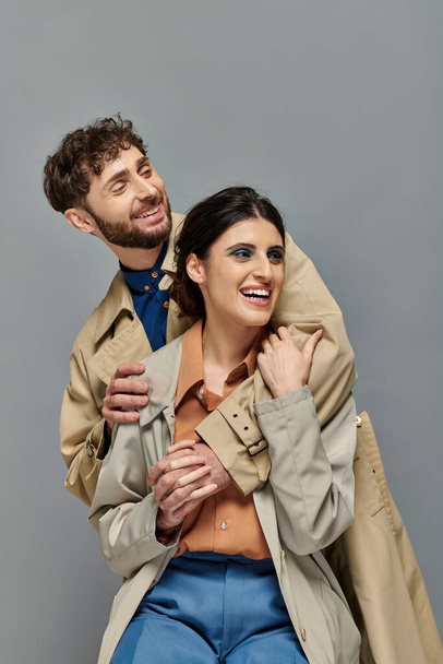 cheerful couple, outerwear, fall season, grey background, man and woman in trench coats, style - Photo, Image