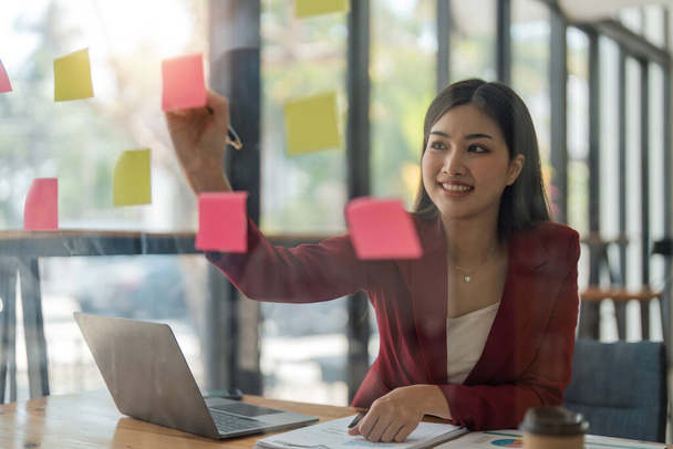 business female write down on colorful sticky notes manage list, concentrated business woman work on startup brainstorm collaborate plan on stickers on glass wall. - Fotoğraf, Görsel