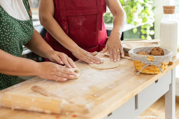 close-up das mãos de duas mulheres com seus aventais amassar massa na cozinha. preparando alguma sobremesa - Foto, Imagem