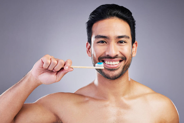 Smile, portrait and a man brushing teeth on a studio background for cleaning, grooming and hygiene. Happy, wellness and an Asian person with a toothbrush for care of mouth isolated on a backdrop. - Photo, Image