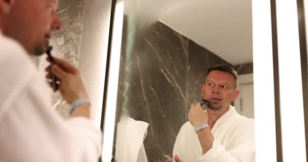 Spiegelbild eines jungen Mannes mit Rasiermesser reinigt die Haare. Zufrieden gutaussehend kerl genießen morgen routine - Filmmaterial, Video