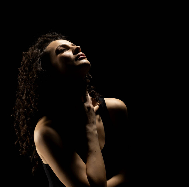 Портрет женщины в тени, держать ее шею, закрытые глаза на черном фоне студии - Фото, изображение