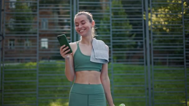 Спортсменка відповідає на повідомлення на мобільному телефоні на спортивному полі - Кадри, відео