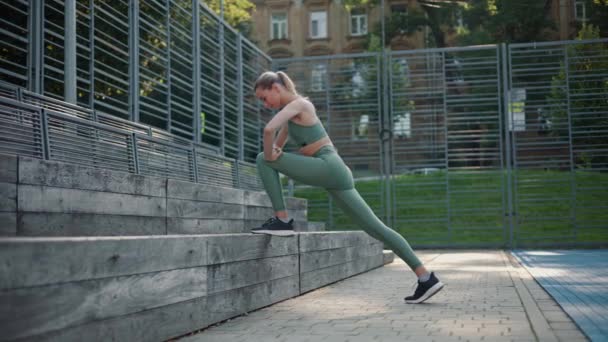 Belle fille sportive fait des étirements de jambe, s'appuyant sur un banc en bois extérieur - Séquence, vidéo