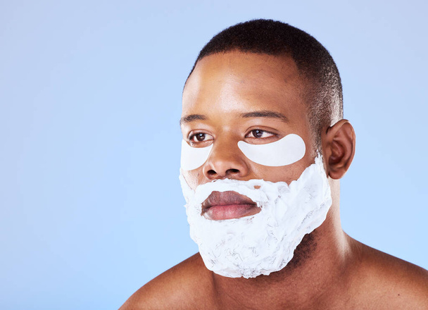 Skincare, black man and eye mask while shaving in studio cleaning, cosmetic or treatment on blue background. Face, beauty and African guy model with gel patch and skin for facial, hair or wellness. - Фото, зображення