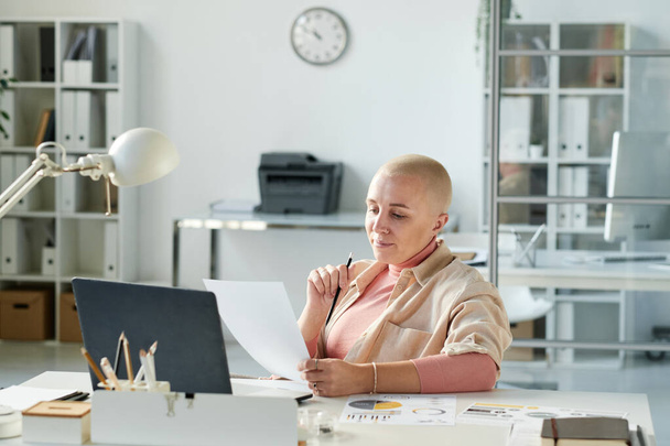 Busy modern Caucasian businesswoman with bald hairstyle sitting at office desk and working with papers - Fotó, kép