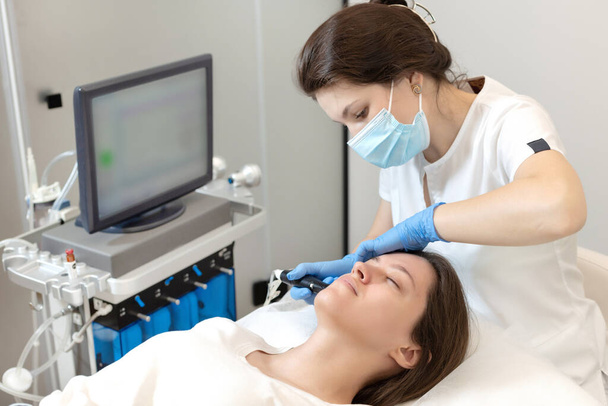 Smart skilled cosmetologist using a modern device while doing hydrafacial procedure - Foto, immagini