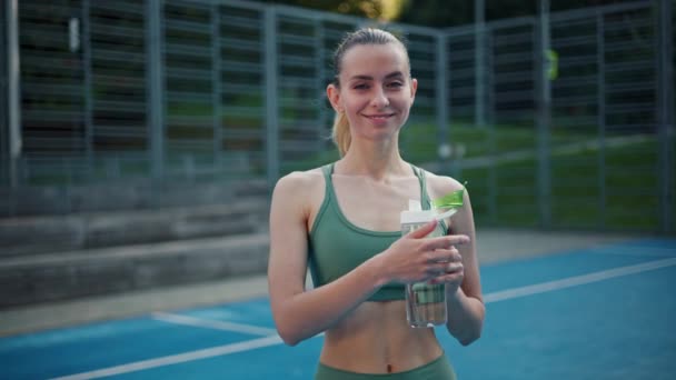 Athletic girl drinks water from sport bottle on the sports field - Footage, Video
