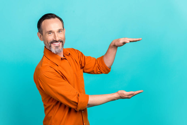 Photo of cheerful positive man dressed orange shirt showing arms size empty space isolated turquoise color background. - Photo, Image