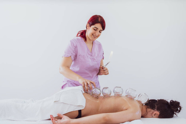 Terapeuta profissional fazendo tratamento hijama nas costas do paciente. Colocando copos de vácuo aquecidos para curar a dor crônica. - Foto, Imagem