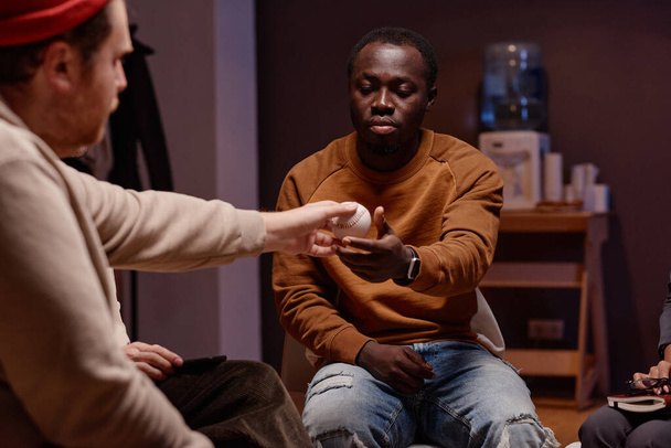 Horizontal shot of young Caucasian man passing ball to African American man during group therapy session - Valokuva, kuva
