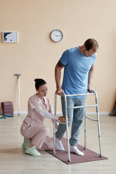 Imagen vertical del paciente tratando de caminar con el caminante y el médico ayudándole durante su rehabilitación - Foto, imagen