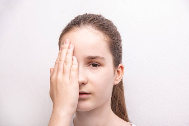 όραση μάτι και θεραπεία όρασης, κορίτσι κρύψει ένα μάτι πίσω από την παλάμη πάνω από λευκό χρώμα υφή τοίχου με αντίγραφο χώρο - Φωτογραφία, εικόνα