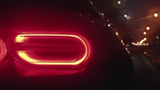 Luce di coda di un'auto sportiva nera parcheggiata in strada che brilla nel buio di una città notturna - Filmati, video